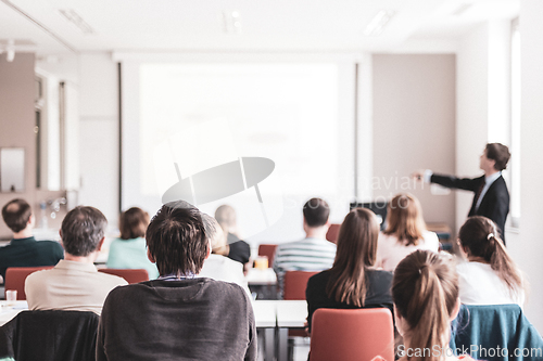 Image of Speaker giving presentation in lecture hall at university. Participants listening to lecture and making notes