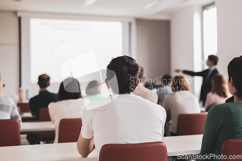 Image of Speaker giving presentation in lecture hall at university. Participants listening to lecture and making notes