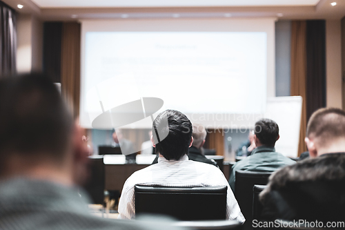 Image of Business and entrepreneurship symposium. Speaker giving a talk at business meeting. Audience in the conference hall. Rear view of unrecognized participant in audience