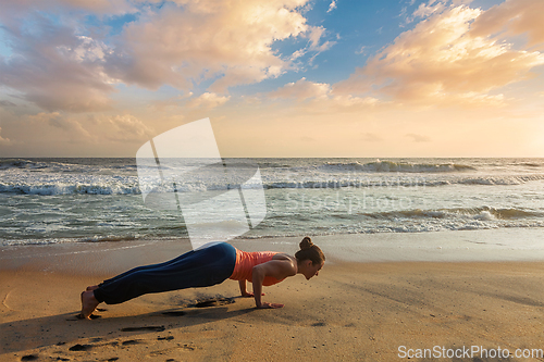 Image of Woman practices yoga at the beach on sunset