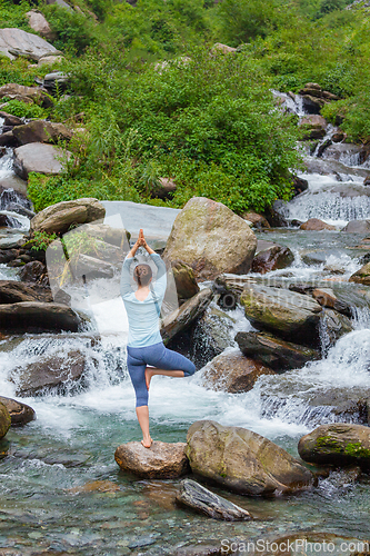 Image of Woman in yoga asana Vrikshasana tree pose at waterfall outdoors