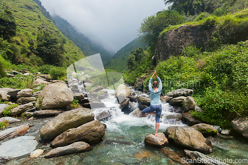 Image of Woman in yoga asana Vrikshasana tree pose at waterfall outdoors