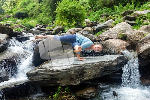 Image of Woman doing yoga oudoors at tropical waterfall