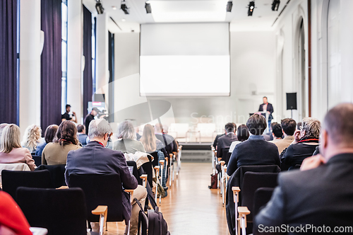 Image of Speaker giving a talk in conference hall at business event. Rear view of unrecognizable people in audience at the conference hall. Business and entrepreneurship concept.