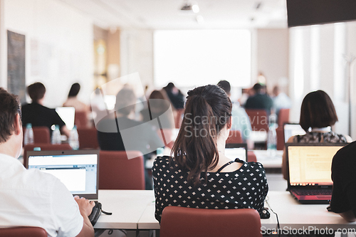 Image of Speaker giving presentation in lecture hall at university. Participants listening to lecture and making notes