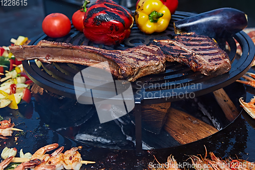 Image of Tomahawk rib beef steak and T-bone on hot black grill.