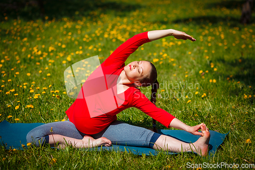 Image of Pregnant woman doing asana Parivrtta Janu Sirsasana outdoors