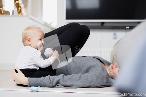 Image of Happy family moments. Mother lying comfortably on children's mat playing with her baby boy watching and suppervising his first steps. Positive human emotions, feelings, joy.