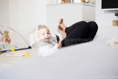 Image of Happy family moments. Mother lying comfortably on children's mat playing with her baby boy watching and suppervising his first steps. Positive human emotions, feelings, joy.