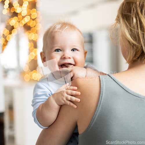 Image of Blonde mother holding her adorable cheerful little infant baby boy. Cute infant child looking in camera and smiling at home.