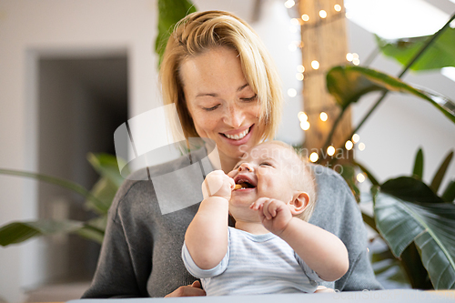 Image of Portrait of young mother cuddling her adorable little child while sitting at the table at home. Sensory stimulation for baby development