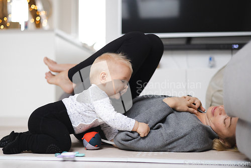 Image of Happy family moments. Mother lying comfortably on children's mat playing with her baby boy watching and suppervising his first steps. Positive human emotions, feelings, joy.