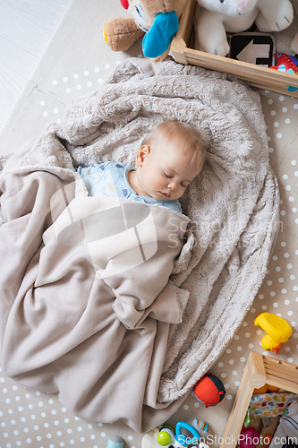 Image of Cute infant baby boy sleeping on playing mat covered with warm cosy blanket.