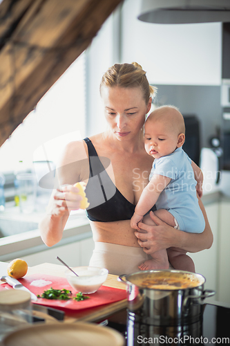 Image of Woman cooking while holding four months old baby boy in her hands