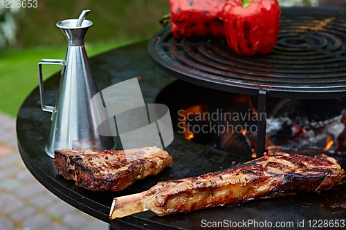 Image of Tomahawk rib beef steak and T-bone on hot black grill.