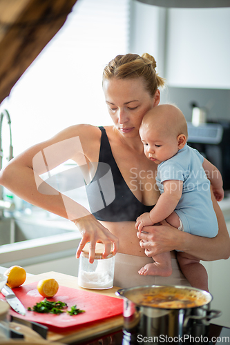 Image of Woman cooking while holding four months old baby boy in her hands