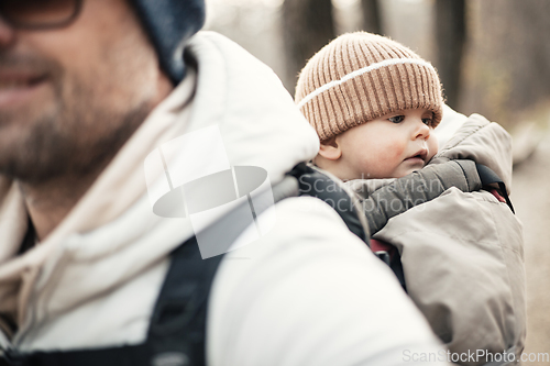 Image of Sporty father carrying his infant son wearing winter jumpsuit and cap in backpack carrier hiking in autumn forest.