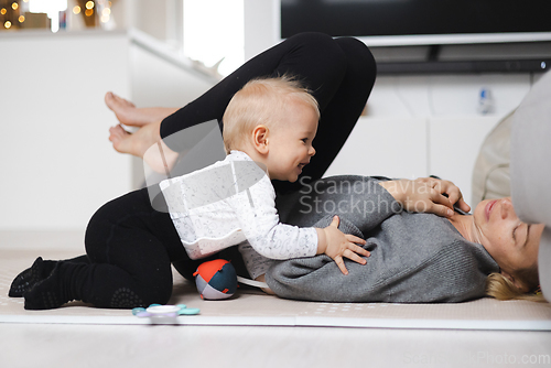 Image of Happy family moments. Mother lying comfortably on children's mat playing with her baby boy watching and suppervising his first steps. Positive human emotions, feelings, joy.