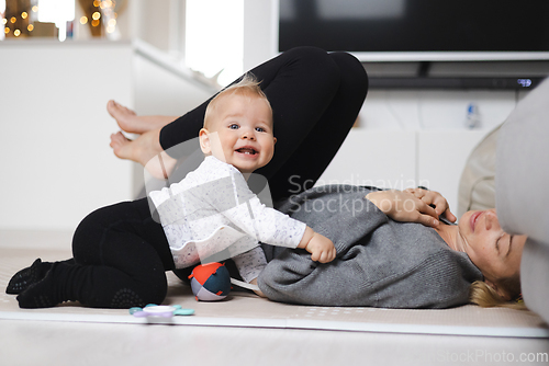 Image of Happy family moments. Mother lying comfortably on children's mat playing with her baby boy watching and suppervising his first steps. Positive human emotions, feelings, joy.