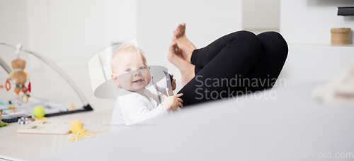 Image of Happy family moments. Mother lying comfortably on children's mat playing with her baby boy watching and suppervising his first steps. Positive human emotions, feelings, joy.