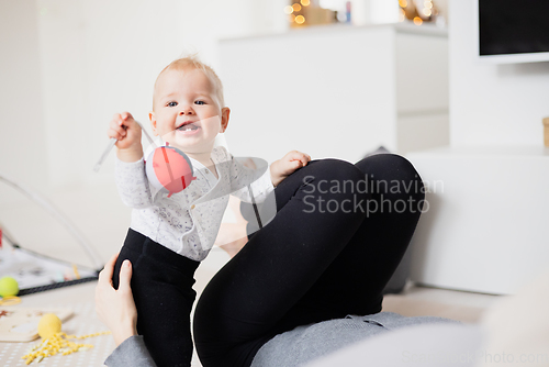 Image of Happy family moments. Mother lying comfortably on children's mat watching and suppervising her baby boy playinghis in living room. Positive human emotions, feelings, joy