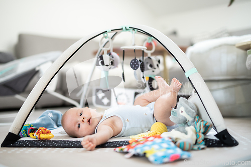 Image of Cute baby boy playing with hanging toys arch on mat at home Baby activity and play center for early infant development. Baby playing at home