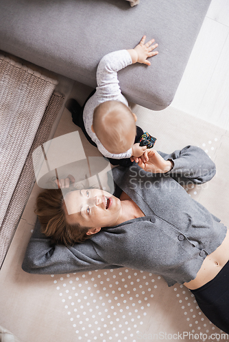 Image of Happy family moments. Mother lying comfortably on children's mat playing with her baby boy watching and suppervising his first steps. Positive human emotions, feelings, joy.