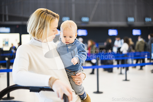 Image of Motherat travelling with his infant baby boy child, walking, pushing baby stroller and luggage cart at airport terminal station. Travel with child concept.