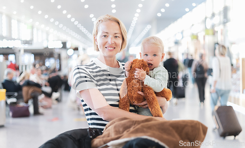 Image of Mother traveling with child, holding his infant baby boy at airport terminal waiting to board a plane. Travel with kids concept.