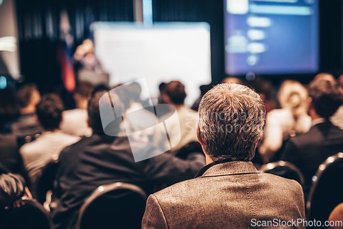 Image of Speaker giving a talk in conference hall at business event. Rear view of unrecognizable people in audience at the conference hall. Business and entrepreneurship concept.