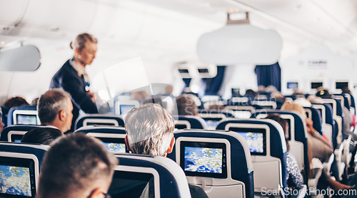 Image of Interior of airplane with passengers on seats and stewardess in uniform walking the aisle, serving people. Commercial economy flight service concept.