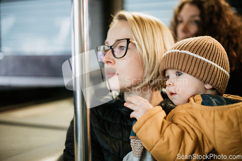 Image of Mother carries her child while standing and holding on to the bus. Mom holding her infant baby boy in her arms while riding in a public transportation. Cute toddler boy traveling with his mother.