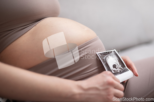 Image of Pregnant woman belly. Pregnancy Concept. Pregnant tummy close up. Detail of pregnant woman relaxing on comfortable sofa at home.