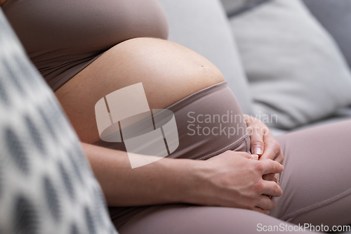 Image of Pregnant woman belly. Pregnancy Concept. Pregnant tummy close up. Detail of pregnant woman relaxing on comfortable sofa at home.