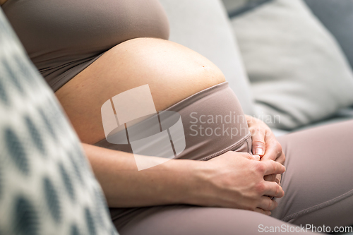 Image of Pregnant woman belly. Pregnancy Concept. Pregnant tummy close up. Detail of pregnant woman relaxing on comfortable sofa at home.