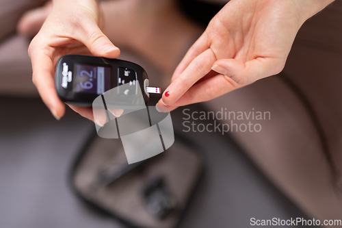 Image of Blood sugar testing at home. Woman checking blood sugar level by glucometer and test stripe at home. Diabetic checking blood sugar levels.