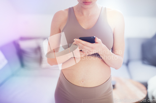 Image of Close-up photo of pregnant female belly. Woman holding and using mobile smart phone application at home interiors. Pregnancy, technology, online shopping, preparation and expectation concept.