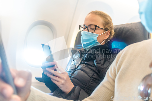 Image of A young couple wearing face mask, using smart phone while traveling on airplane. New normal travel after covid-19 pandemic concept.