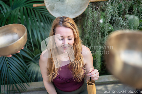 Image of Yoga concept, meditation and sound therapy. Beautiful young caucasian woman surrounded by copper tibetan singing bowls and instruments.