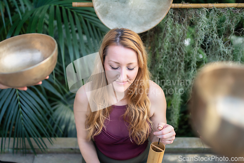 Image of Yoga concept, meditation and sound therapy. Beautiful young caucasian woman surrounded by copper tibetan singing bowls and instruments.