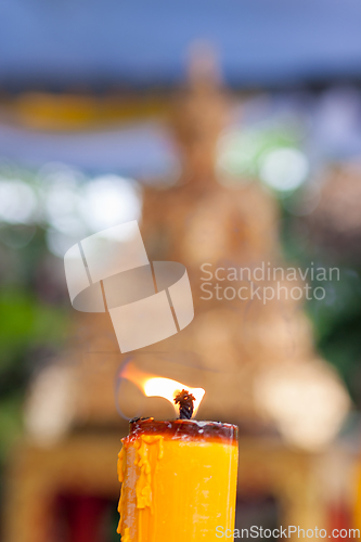 Image of Candlelight burning in front of Buddha statue. Focus on candle frame, buddha blured in background.