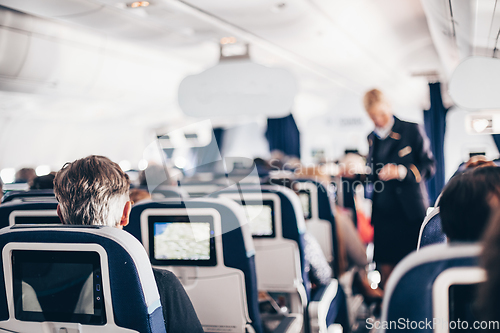 Image of Interior of airplane with passengers on seats and stewardess in uniform walking the aisle, serving people. Commercial economy flight service concept.