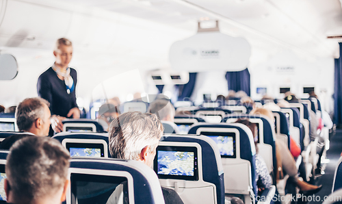 Image of Interior of airplane with passengers on seats and stewardess in uniform walking the aisle, serving people. Commercial economy flight service concept.