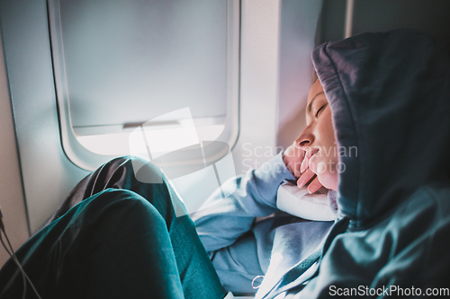 Image of Tired blonde casual caucasian woman wearing sporty hoodie napping on seat while traveling by airplane. Commercial transportation by planes. Authentic image of real people.