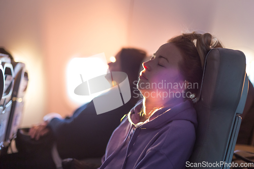 Image of Out of fokus image of tired blonde casual caucasian woman wearing sporty hoodie napping on seat while traveling by airplane. Commercial transportation by planes. Authentic image of real people.