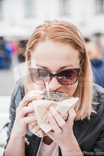 Image of Pretty young blonde funny woman eating hamburger outdoor on the street