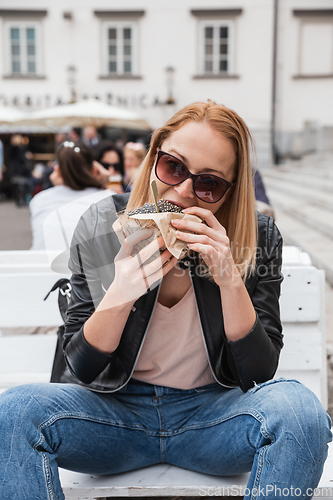 Image of Pretty young blonde funny woman eating hamburger outdoor on the street