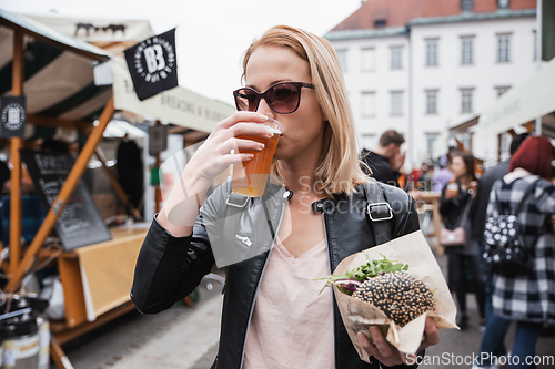 Image of Beautiful young woman holding delicious organic salmon vegetarian burger and drinking homebrewed IPA beer on open air beer an burger urban street food festival in Ljubljana, Slovenia.