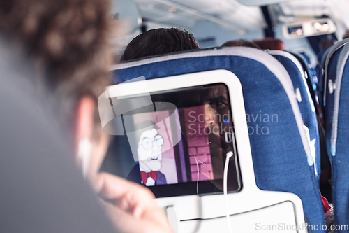 Image of Reflection of a passenger on an airplane touch screen monitor while watching cartoon during long flight. Entertainment service system in aircraft.
