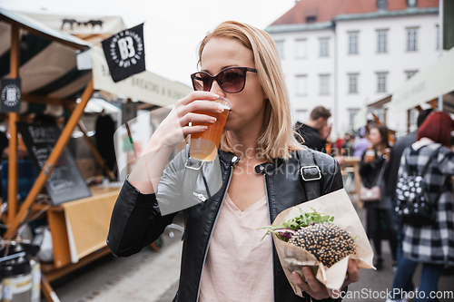 Image of Beautiful young woman holding delicious organic salmon vegetarian burger and drinking homebrewed IPA beer on open air beer an burger urban street food festival in Ljubljana, Slovenia.